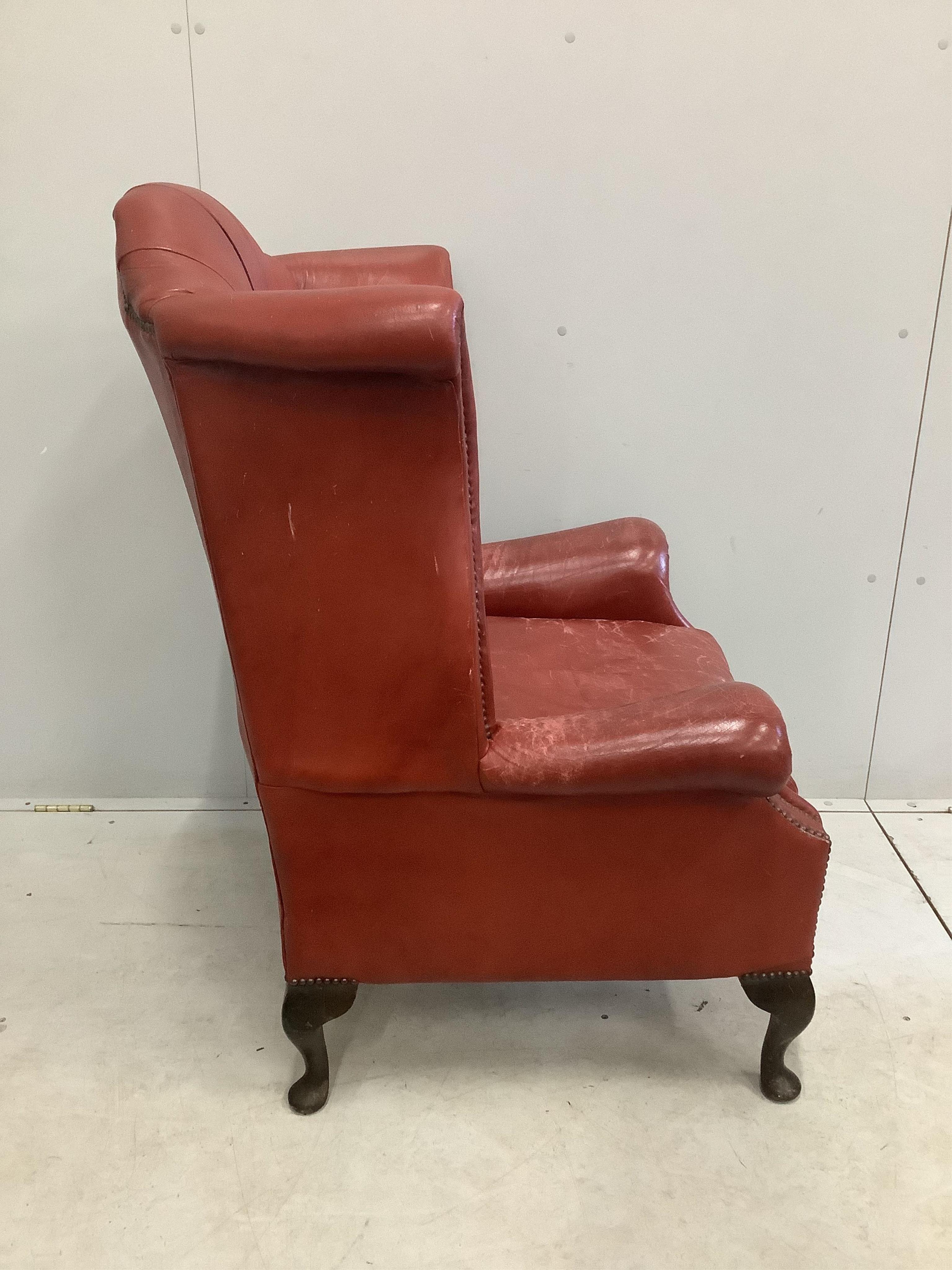 A Georgian style wing armchair with brick red leather upholstery, width 86cm, height 112cm. Condition - fair, but wear to the tops of the arms and seat